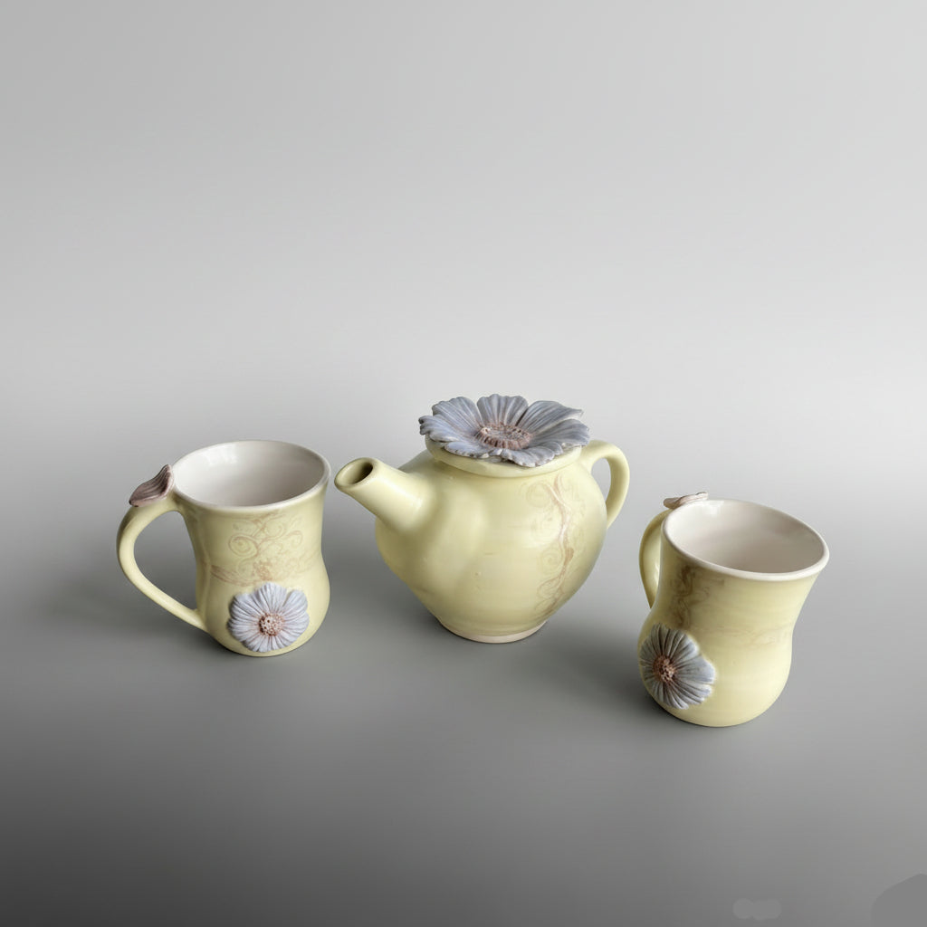 Set of ceramic teapot and mugs with floral designs on a semi opaque primrose yellow base
