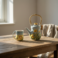 Ceramic teapot and mug with flowers on a sunny English countryside field, Shiny bright glaze in Stoneware.